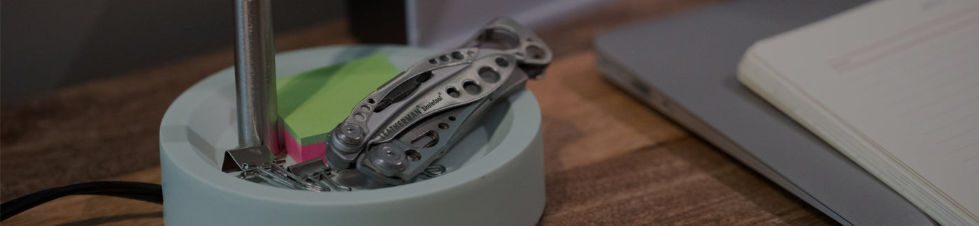 Translation missing: en.Stainless Steel Leatherman Skeletool® resting on a desk organizer beside a notebook and sticky notes in a modern workspace.