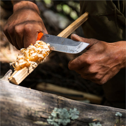 Translation missing: en.Person using a Leatherman Pioneer knife to carve feather sticks from a wooden branch in an outdoor setting, shown in a close-up highlighting controlled bushcraft technique