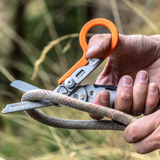 Translation missing: en.A man using an orange and black Leatherman Raptor Rescue shears to cut a thick rope