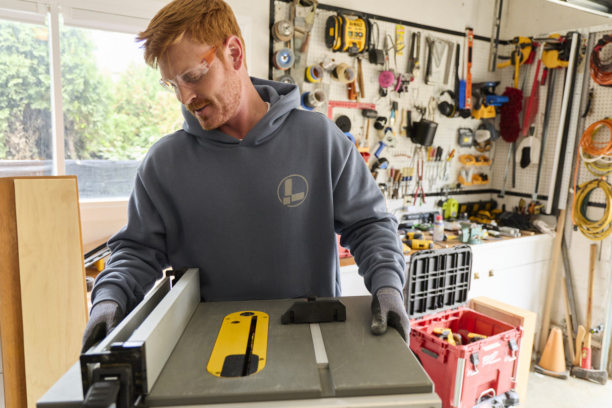 Translation missing: en.A person wearing a storm blue Leatherman Classic Hoodie standing in front of a woodworking tool in a garage workshop