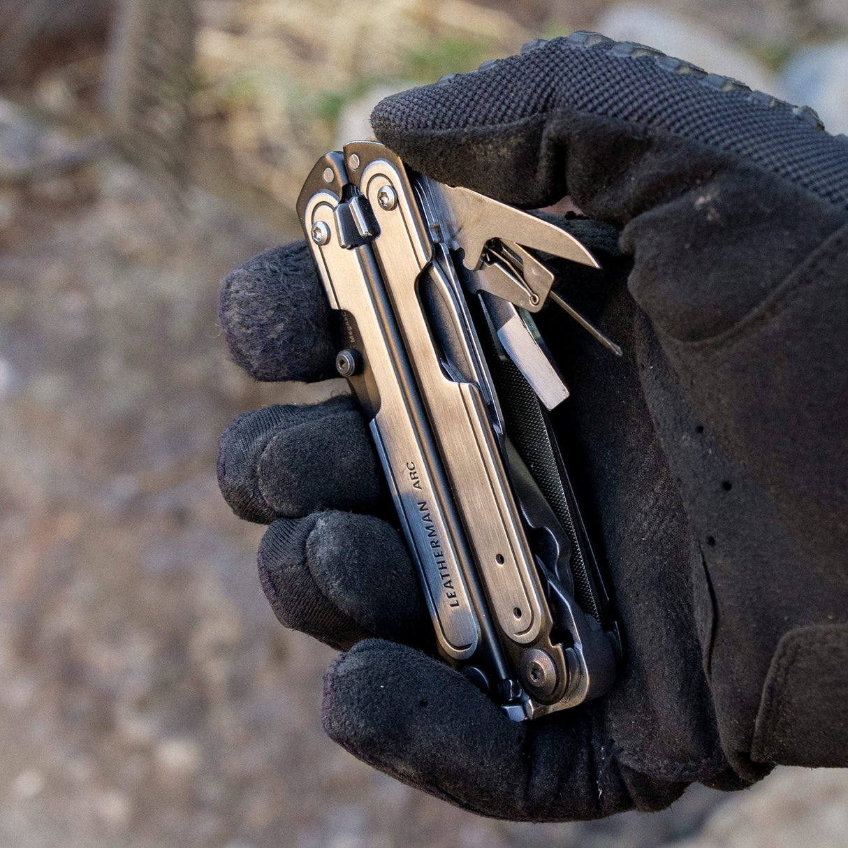 Translation missing: en.Black DLC & Stainless Steel Leatherman ARC® held in a gloved hand, showcasing some tool included tools