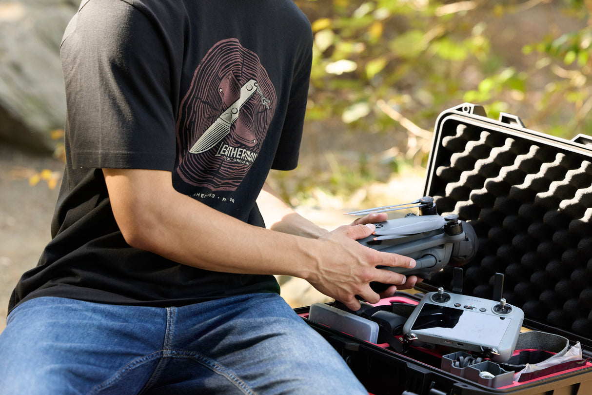 Translation missing: en.A person pulling a drone out of a carrying case while wearing a black Leatherman Blade & Grain Tee with a fixed blade design on the front