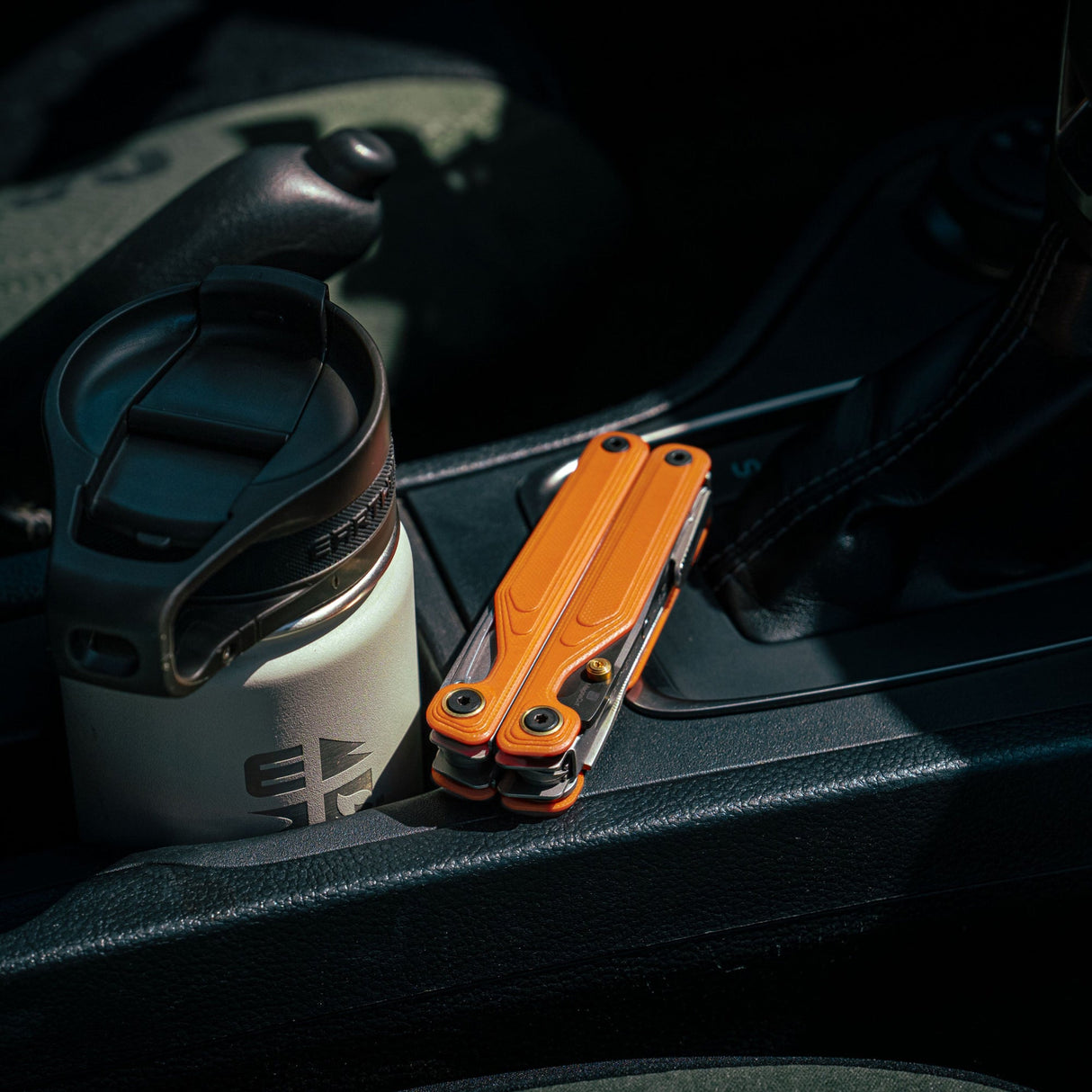 Translation missing: en.Canyonland Leatherman Wave® Alpha multitool beside a stainless steel coffee mug in a car