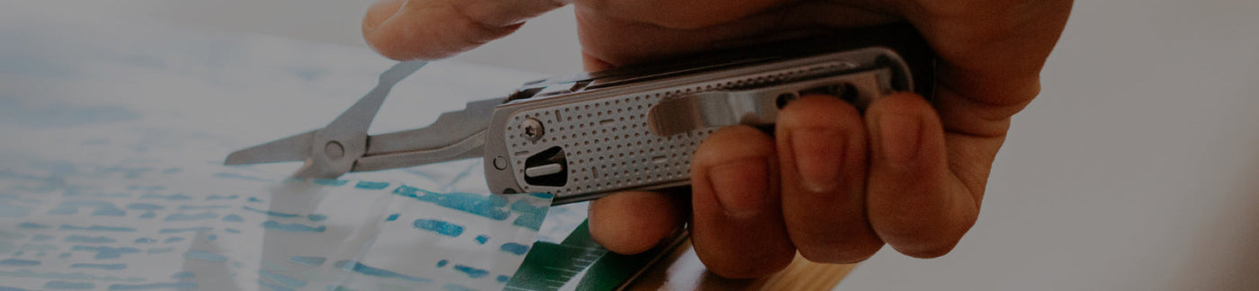 Translation missing: en.Hand holding Leatherman Free T2 with scissors opened, being used to cut paper