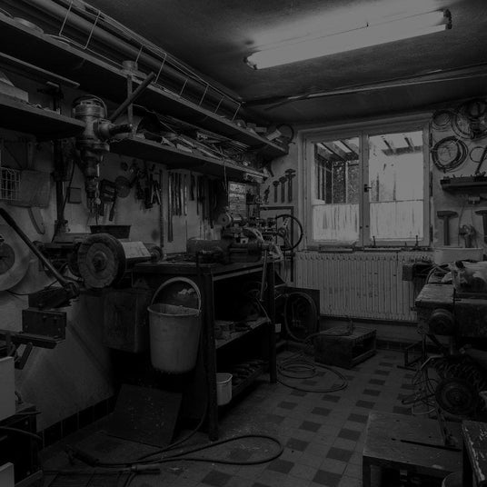 Translation missing: en.Black and white photo of a well-equipped workshop with various tools hanging on the wall, workbenches, and machinery