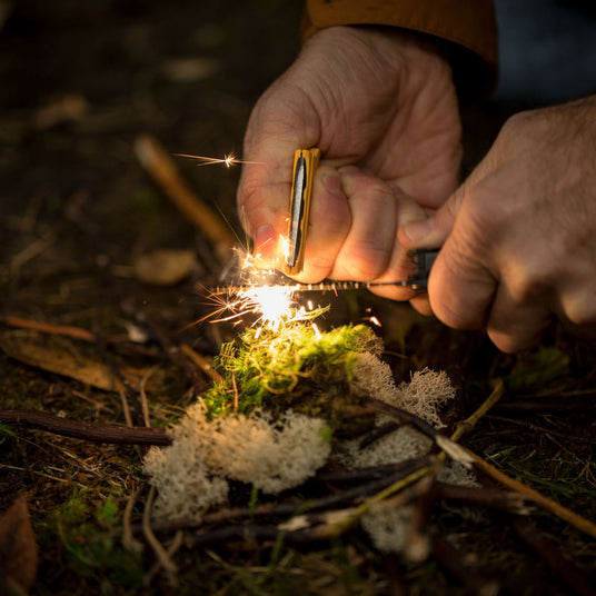 Translation missing: en.Close-up hands using a Leatherman Signal to start a fire in the wilderness with a fire-starting ferro rod