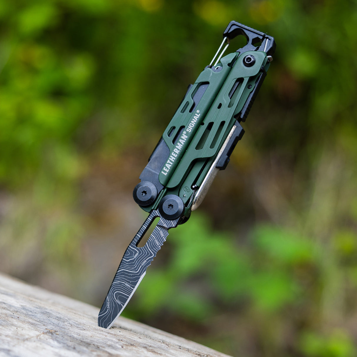 Translation missing: en.Green Leatherman Signal multitool with customized blade open, sticking into a piece of wood outdoors