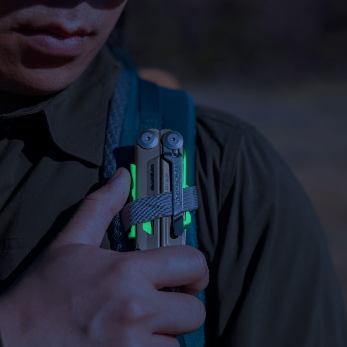 Translation missing: en.Person securing a Sandstorm multitool with neon accents to a backpack strap outdoors