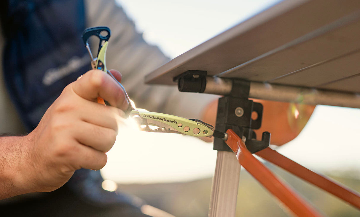 Translation missing: en.Person using a Verdant Leatherman Skeletool® CX multitool on an outdoor table