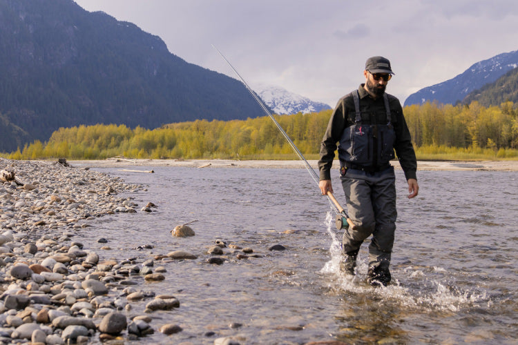 Man with a fishing pole, walking in a river.