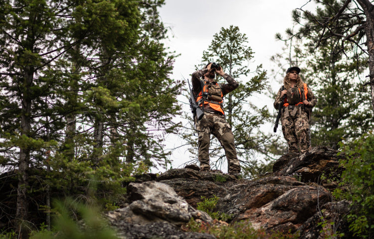 Two hunters on top of a boulder using binoculars to check the terrain