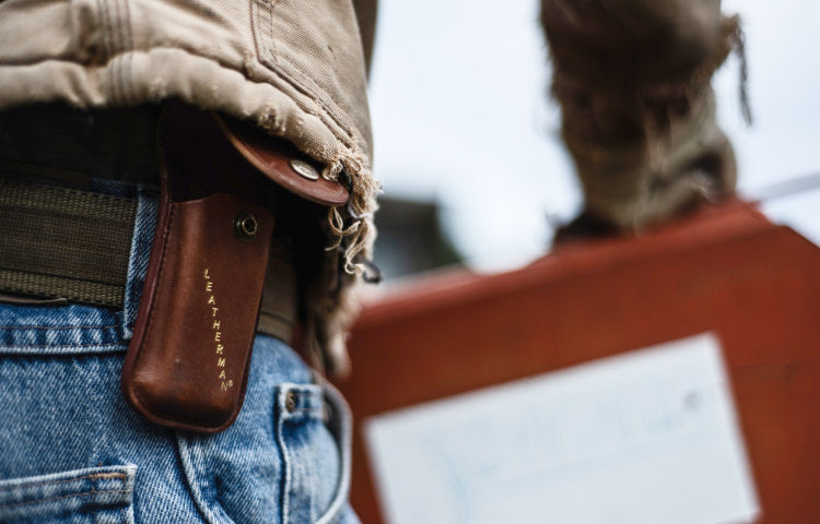 Close-up photo of a person wearing blue denim jeans with a brown Leatherman sheath attached on the belt.