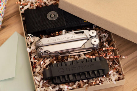 Leatherman Wave closed in a gift box next to a sheath and a bit kit on a table