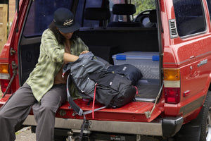 Translation missing: en.A woman wearing a black Leatherman Vintage 5 Panel Hat packing a backpack on the open tailgate of a red vehicle