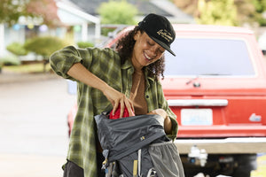 Translation missing: en.A woman wearing a black Leatherman Vintage 5 Panel Hat packing a gray hiking backpack near a red vehicle