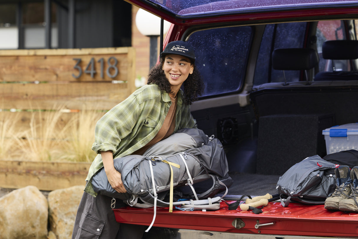Translation missing: en.A woman wearing a black Leatherman Vintage 5-Panel Hat loading camping gear into the back of a red vehicle, smiling while preparing for an outdoor trip