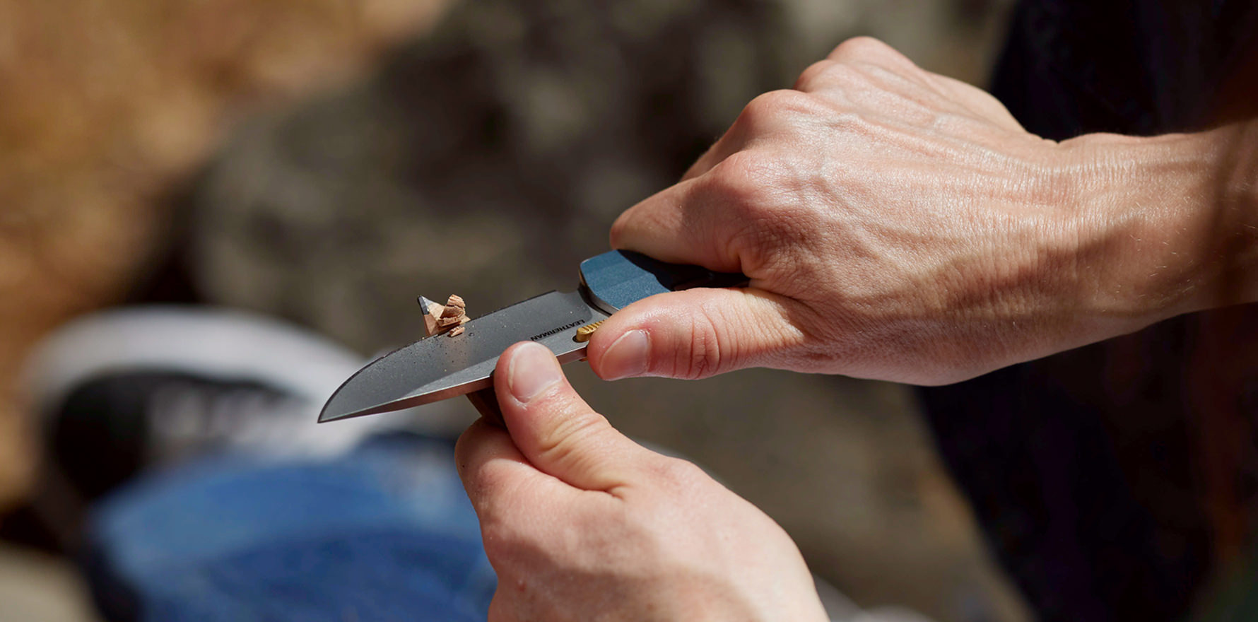 Person using a Leatherman Blazer Denim folding knife to sharpen a pencil outdoors, shown in a close-up with hands in focus during a hands-on task.