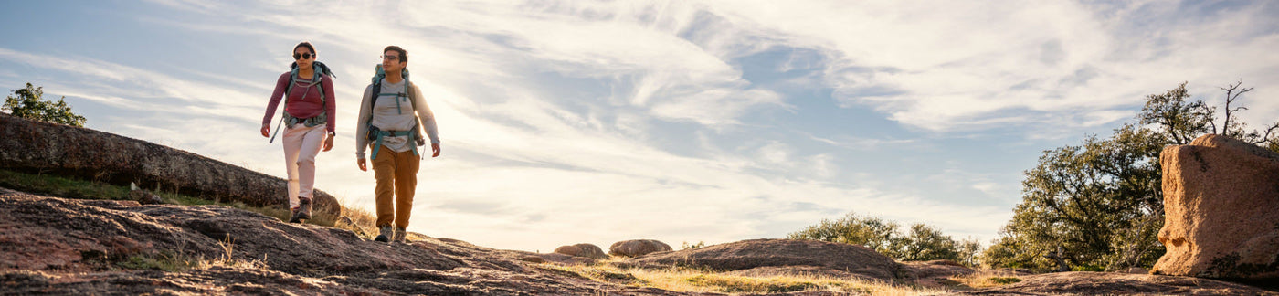 Two hikers wearing backpacks walking through a field