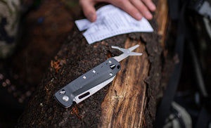 Translation missing: en.Man holding note next to Leatherman K4 with scissors opened on top of tree