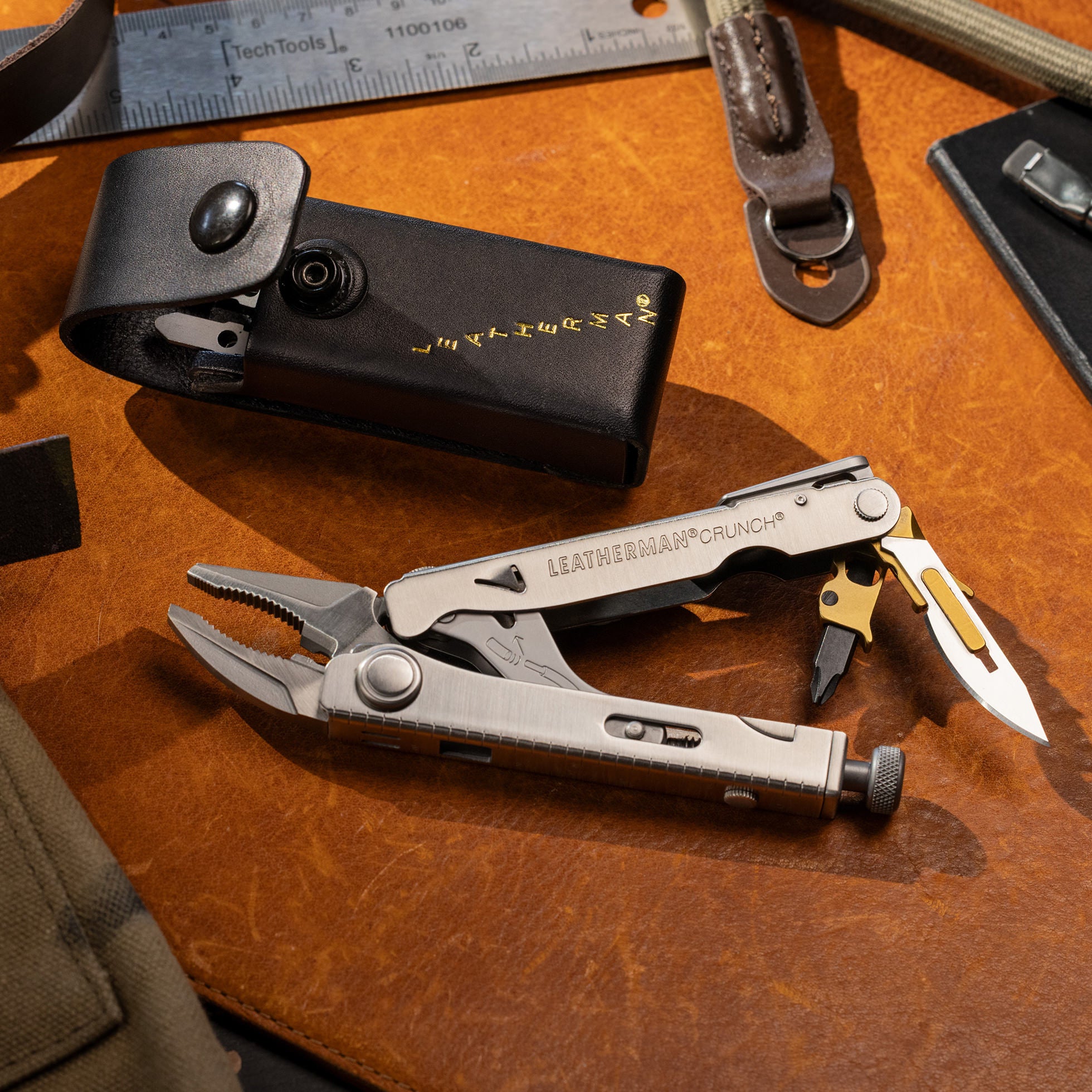 Leatherman Captain's Crunch multitool displayed on a leather surface next to a black leather sheath and other tools.