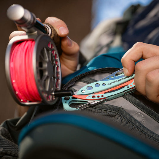 Person pulling Leatherman Skeletool Cx out of blue fishing backpack.