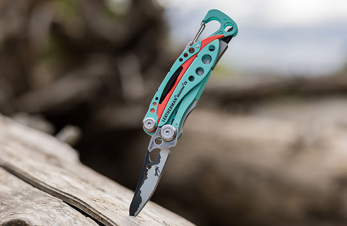 Translation missing: en.Leatherman Skeletool CX inserted in wooden surface, showcasing their metallic finish against the natural wood grain with a customized blade