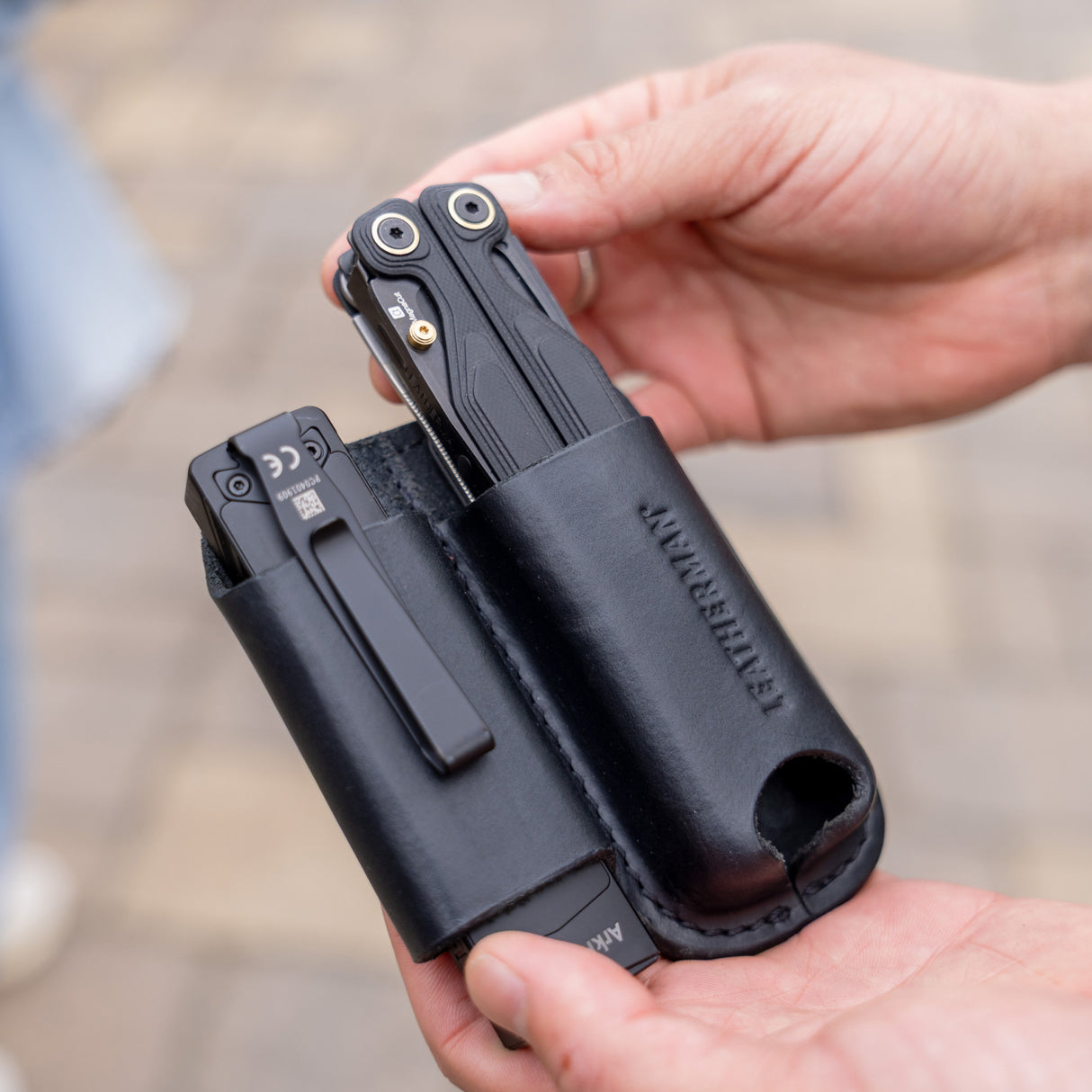 Translation missing: en.Hands holding a black leather sheath carrying two black multitools outdoors