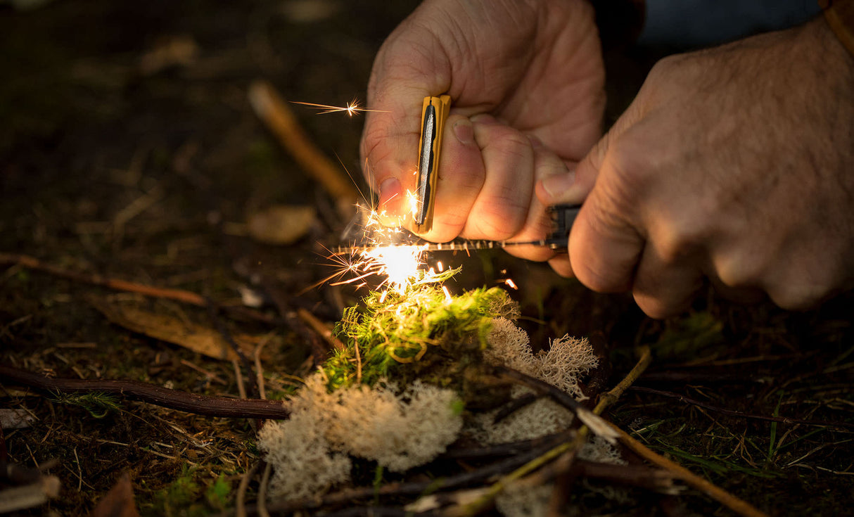 Translation missing: en.A person using the ferro rod on a Leatherman Signal® to create sparks while preparing kindling in the forest