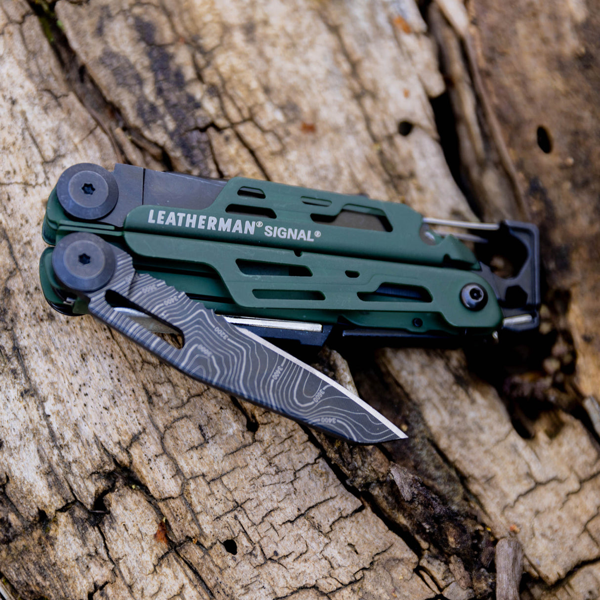 Translation missing: en.Green Leatherman Signal multitool with a customized knife blade resting on weathered wood outdoors