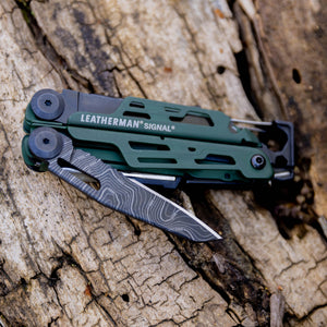 Translation missing: en.Green Leatherman Signal multitool with a customized knife blade resting on weathered wood outdoors