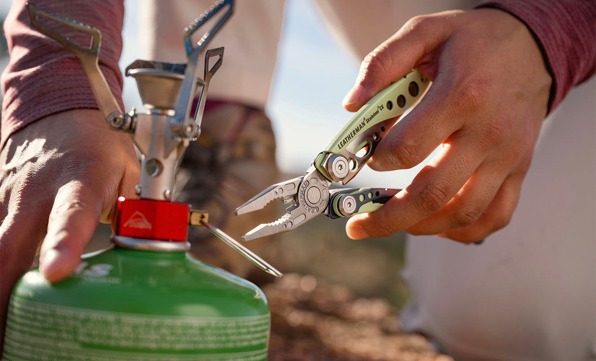 Translation missing: en.Person using a Verdant Leatherman Skeletool® CX multi-tool to adjust a camping stove on a green propane canister