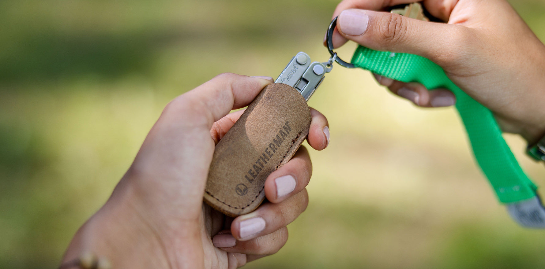 Leatherman Micra on vibrant green keychain being pulled from brown leather tool sleeve