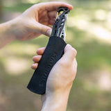 Translation missing: en.A person holding a black leather Leatherman tool sleeve with the Leatherman Skeletool® CX partially inserted; the tool's sleek, stainless steel frame and carabiner clip are visible above the sleeve, which features an embossed "LEATHERMAN" logo