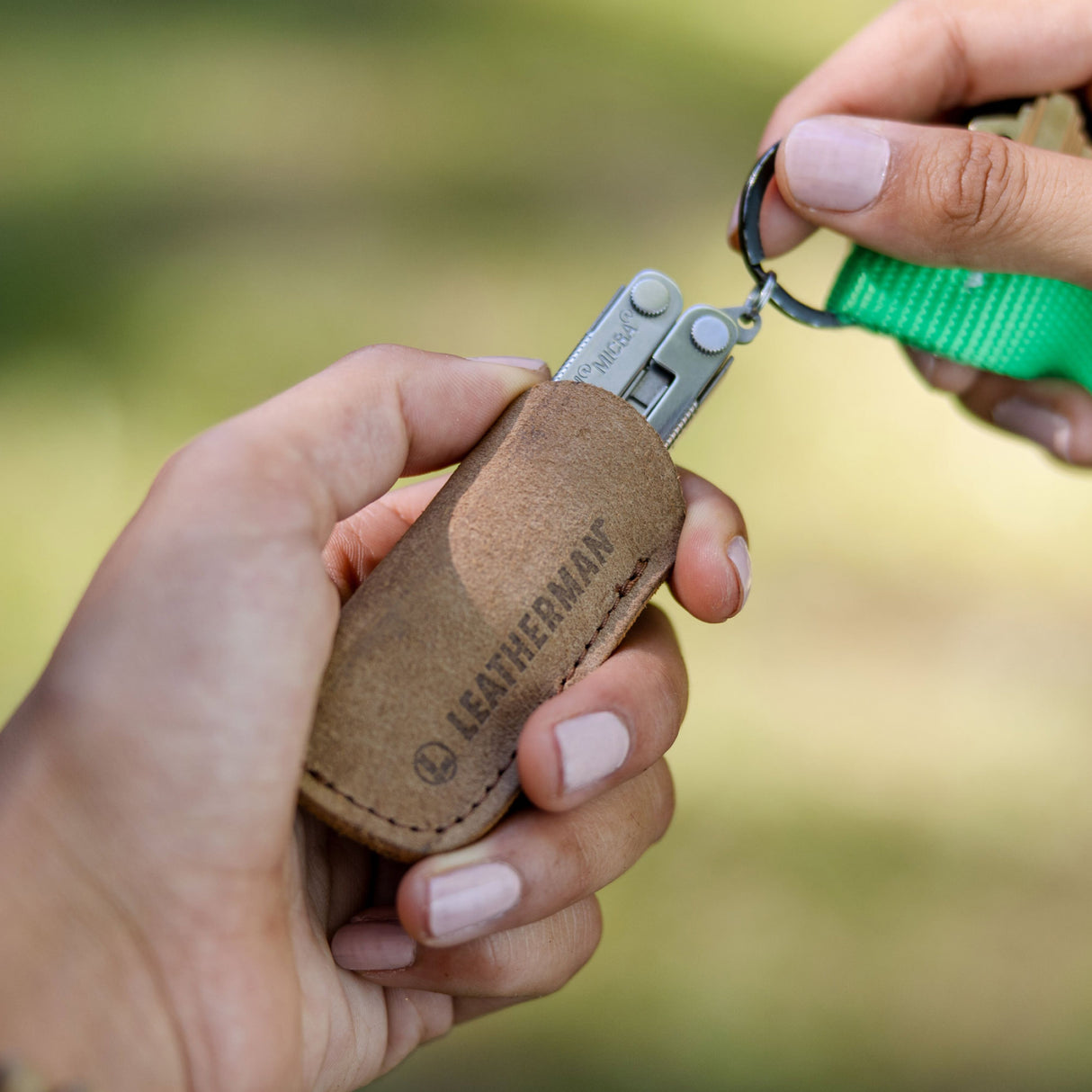 Translation missing: en.Leatherman Micra® on a vibrant green keychain being pulled out of a Micra sized Leatherman brown leather tool sleeve